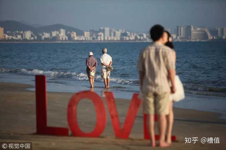 海南三亚湾,夕阳下拍摄婚纱照的情侣,远处是两位老人的背影 视觉