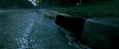 一个小男孩在雨中玩纸船,他追着小船来到下水道口.