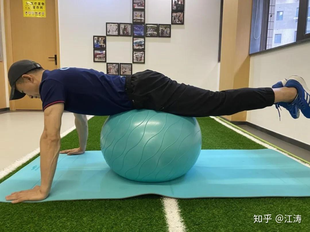 双臂支撑于球前方,腹部贴球训练方法:收紧腹部,保持背部平直,向后踢腿